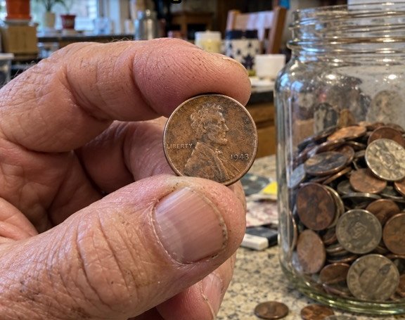 Hand holding an old wheat penny next to a jar of coins